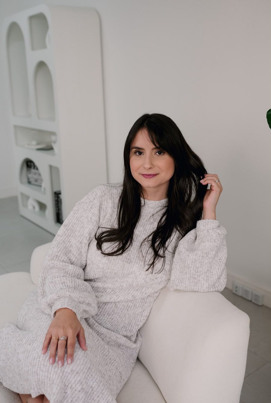 Bruna Almeida sentada em uma poltrona clara, vestindo tricô
